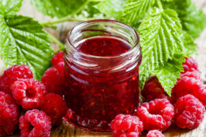 Raspberry jam with fresh raspberries and green leaves on the old
